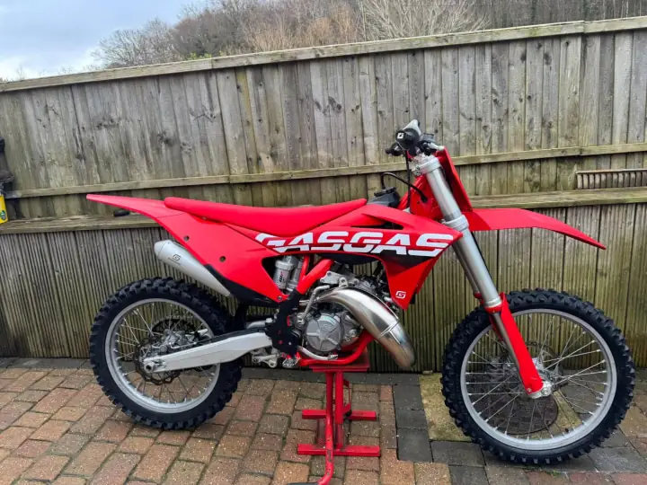 Red GasGas two-stroke motocross bike on a stand in front of a wooden fence