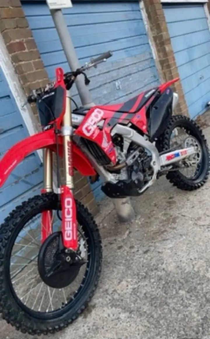 Red Honda CRF motocross bike in race-replica graphics leaning against a row of blue garage doors