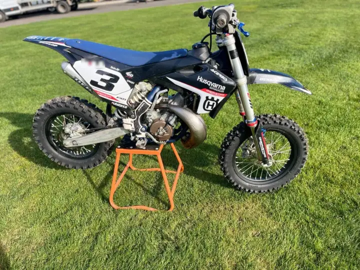 Husqvarna kids' motocross bike in black and white race graphics on an orange stand on a lawn