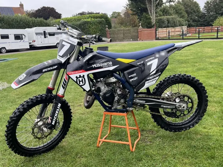Husqvarna two-stroke motocross bike in black race graphics on an orange stand on a lawn