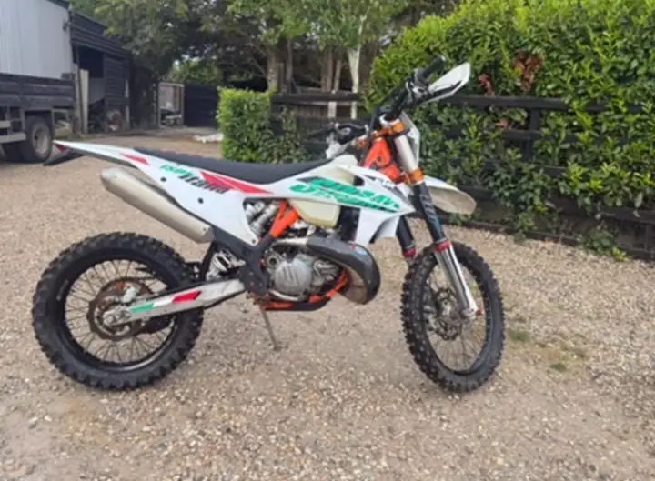 White KTM two-stroke enduro bike with green and red graphics parked side-on on a gravel yard